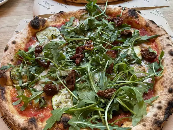 Pizza z rukolą, szynką i płatkami sera na drewnianym stole